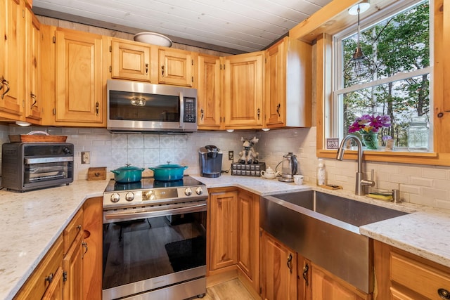 kitchen with backsplash, light stone countertops, sink, and stainless steel appliances