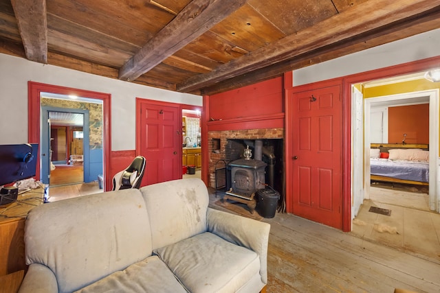 living room with beamed ceiling, wooden ceiling, a wood stove, light hardwood / wood-style floors, and sink