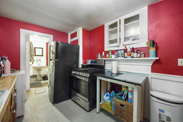 kitchen with black refrigerator, stainless steel range with gas cooktop, and white cabinets