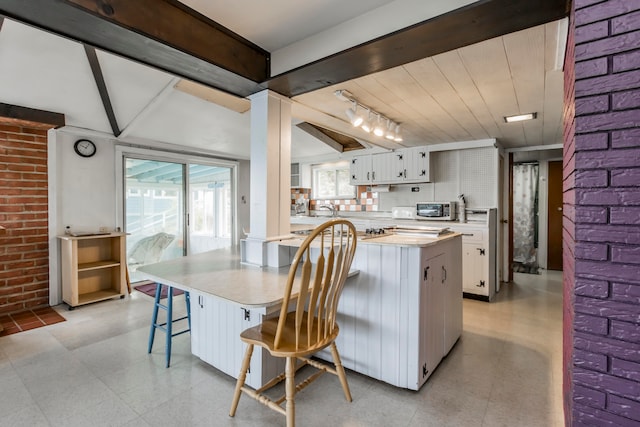 kitchen featuring a kitchen island, white cabinets, brick wall, decorative backsplash, and a breakfast bar area