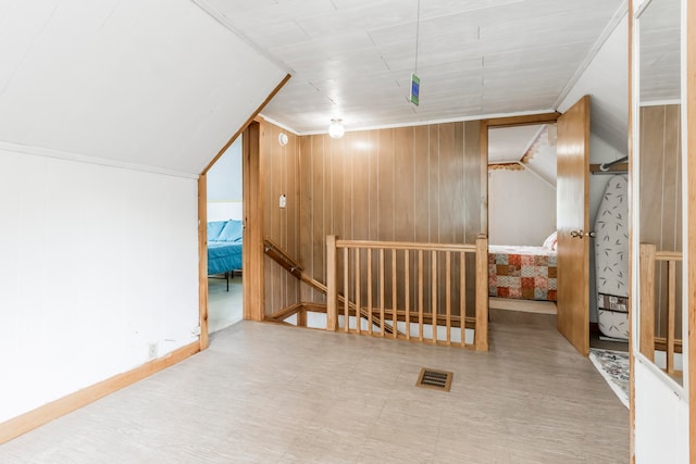 hallway with crown molding, wood walls, and vaulted ceiling