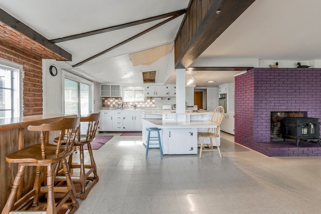 kitchen featuring decorative backsplash, a breakfast bar area, white cabinetry, a wood stove, and brick wall