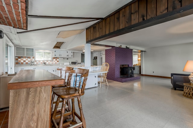 kitchen featuring a kitchen bar, a kitchen island, a wood stove, white cabinetry, and decorative backsplash