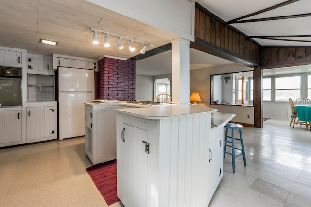 kitchen with a kitchen bar, a center island, black oven, white cabinets, and white fridge