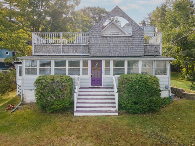 view of front facade with a balcony, a front yard, and a sunroom