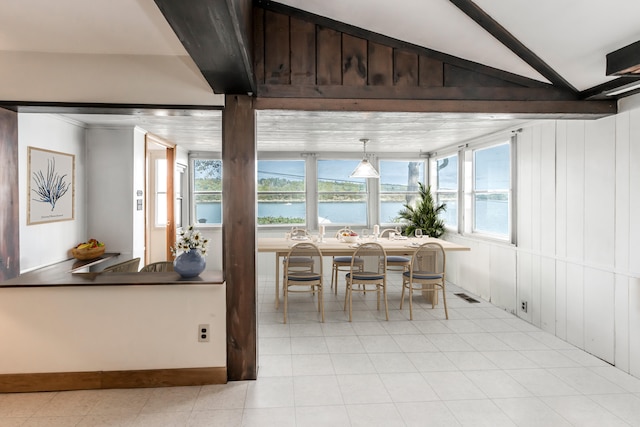 tiled dining space with lofted ceiling and a water view