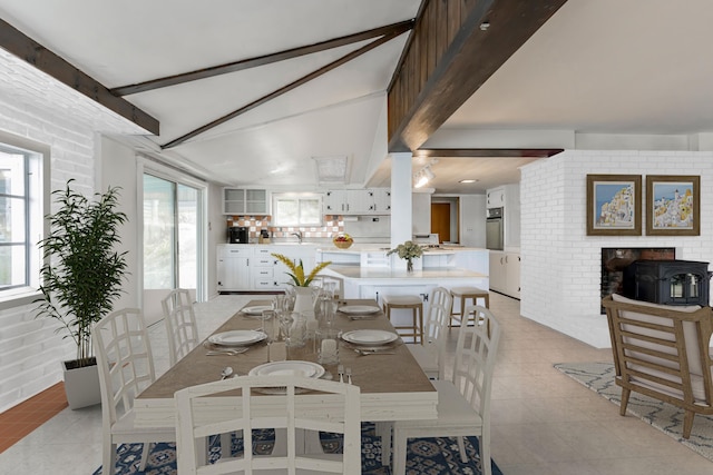 dining area featuring beam ceiling, a healthy amount of sunlight, light tile patterned flooring, and brick wall