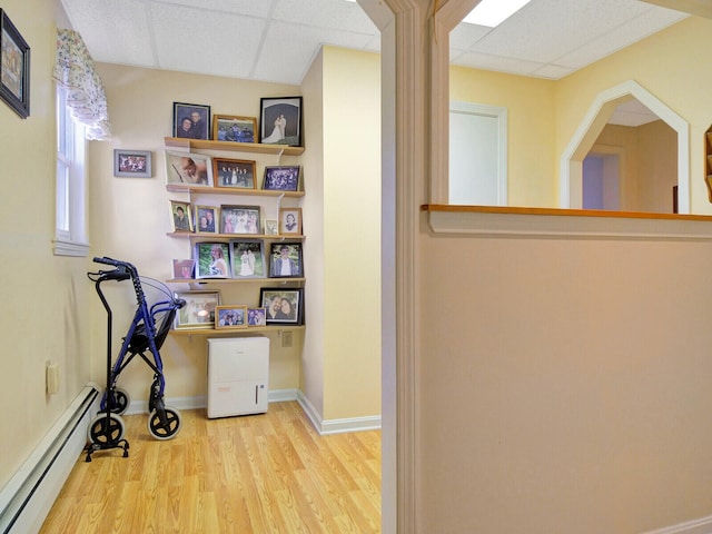 interior space featuring light wood-type flooring, a baseboard radiator, and a drop ceiling