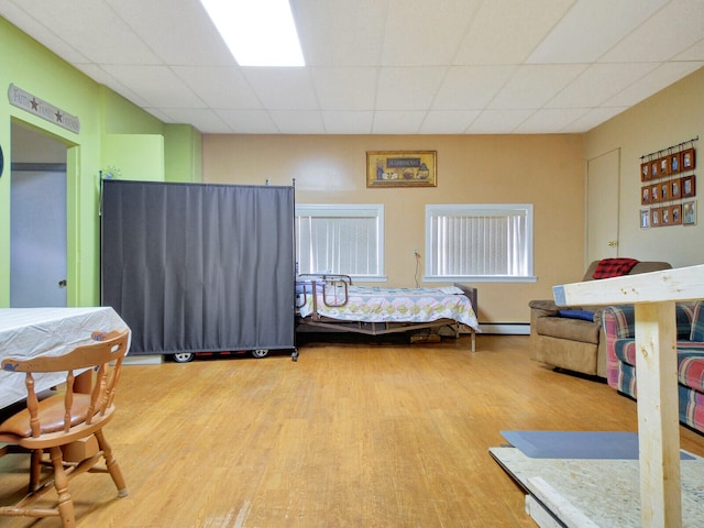 bedroom featuring baseboard heating, wood-type flooring, and a drop ceiling