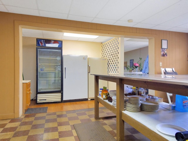 interior space featuring black refrigerator, white fridge, wooden walls, and a drop ceiling