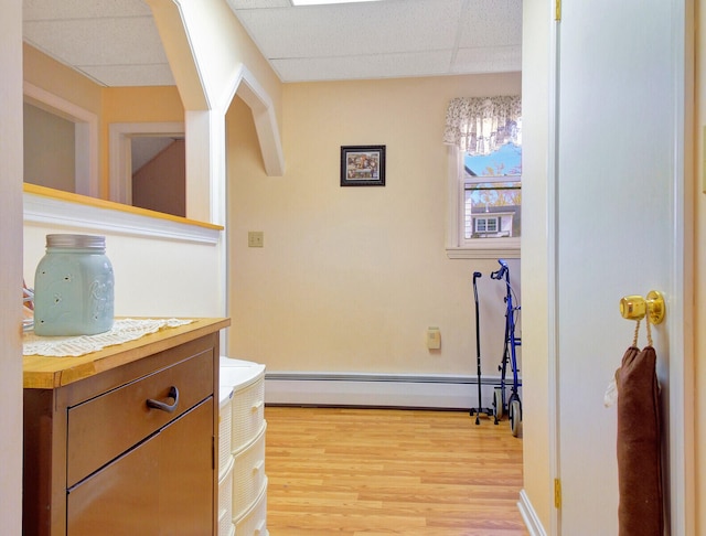 hall with a baseboard heating unit, light wood-type flooring, and a drop ceiling