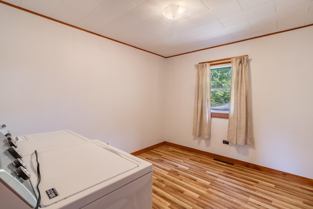 clothes washing area with ornamental molding, washer and clothes dryer, and light wood-type flooring