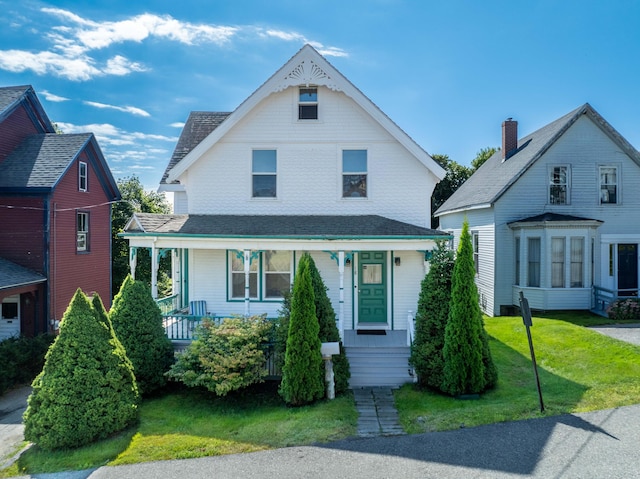 view of front of property featuring covered porch, a shingled roof, and a front lawn