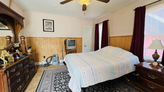 bedroom featuring a wainscoted wall, a ceiling fan, light wood-type flooring, and wooden walls