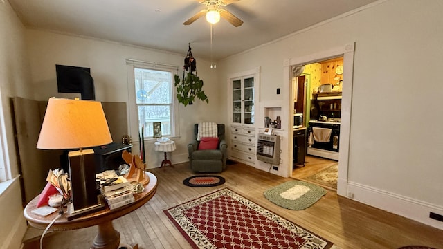 living area featuring hardwood / wood-style floors, heating unit, baseboards, ornamental molding, and ceiling fan