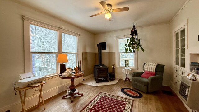 living area featuring hardwood / wood-style flooring, heating unit, crown molding, ceiling fan, and a wood stove