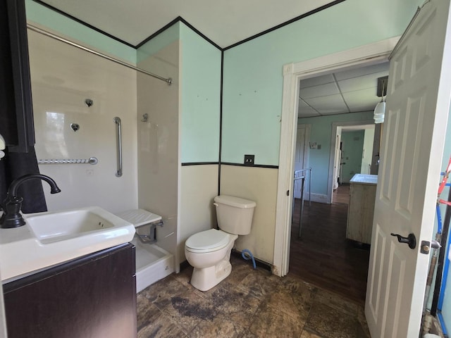 bathroom featuring stone finish flooring, walk in shower, a drop ceiling, toilet, and vanity