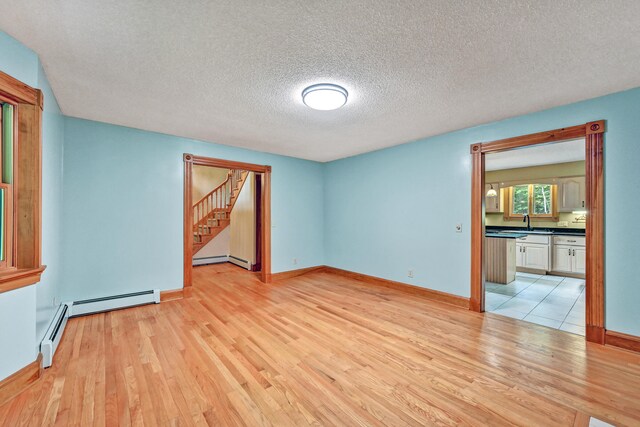 empty room with a baseboard heating unit, sink, a textured ceiling, and light hardwood / wood-style flooring