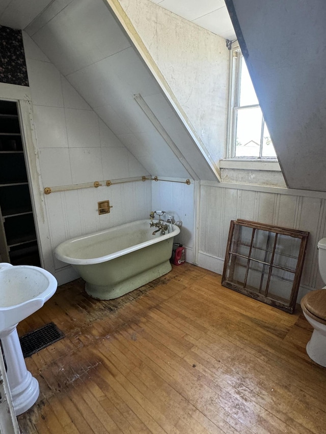 bathroom with lofted ceiling, hardwood / wood-style flooring, toilet, and a tub