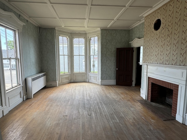 unfurnished living room featuring hardwood / wood-style floors, a brick fireplace, radiator, and a healthy amount of sunlight