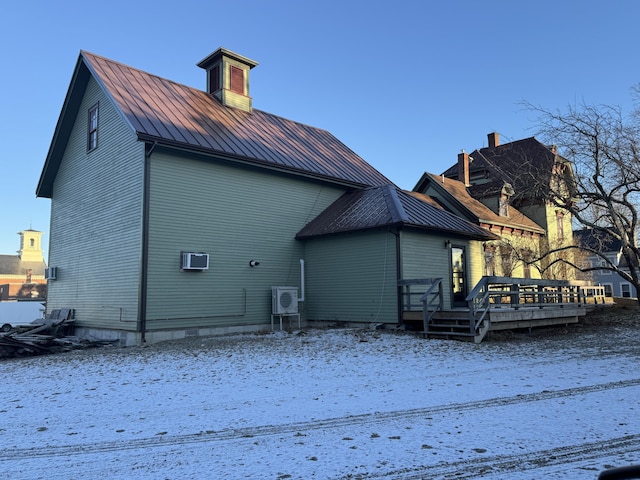 snow covered back of property with a deck and an AC wall unit