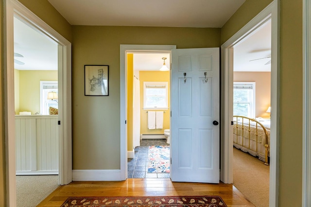 hallway featuring light wood finished floors, plenty of natural light, a baseboard heating unit, and baseboards