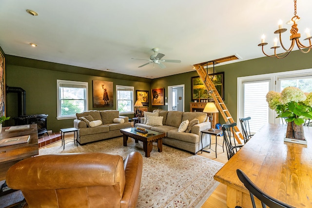 living room featuring ceiling fan with notable chandelier, a wood stove, and light hardwood / wood-style flooring