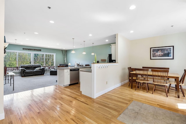 kitchen with light wood-type flooring, white cabinetry, stainless steel dishwasher, and hanging light fixtures