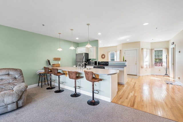 kitchen featuring stainless steel refrigerator, kitchen peninsula, a breakfast bar area, white cabinets, and light hardwood / wood-style floors