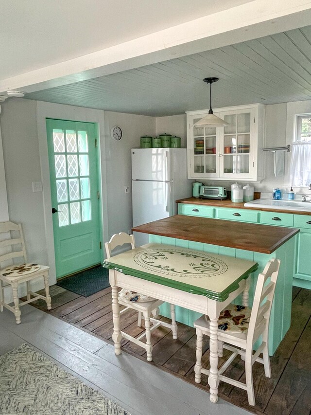 kitchen with freestanding refrigerator, dark wood-type flooring, glass insert cabinets, pendant lighting, and beamed ceiling