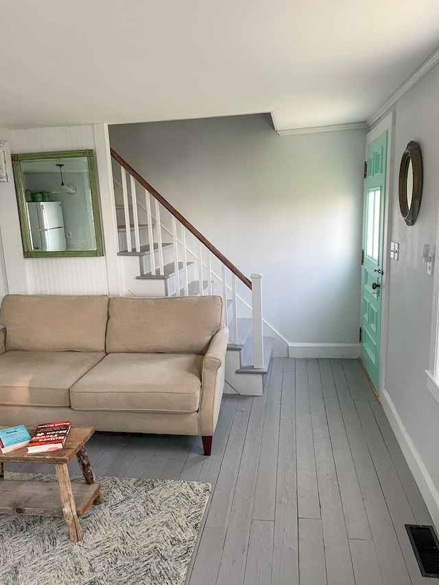 living area featuring hardwood / wood-style floors, stairway, baseboards, visible vents, and ornamental molding