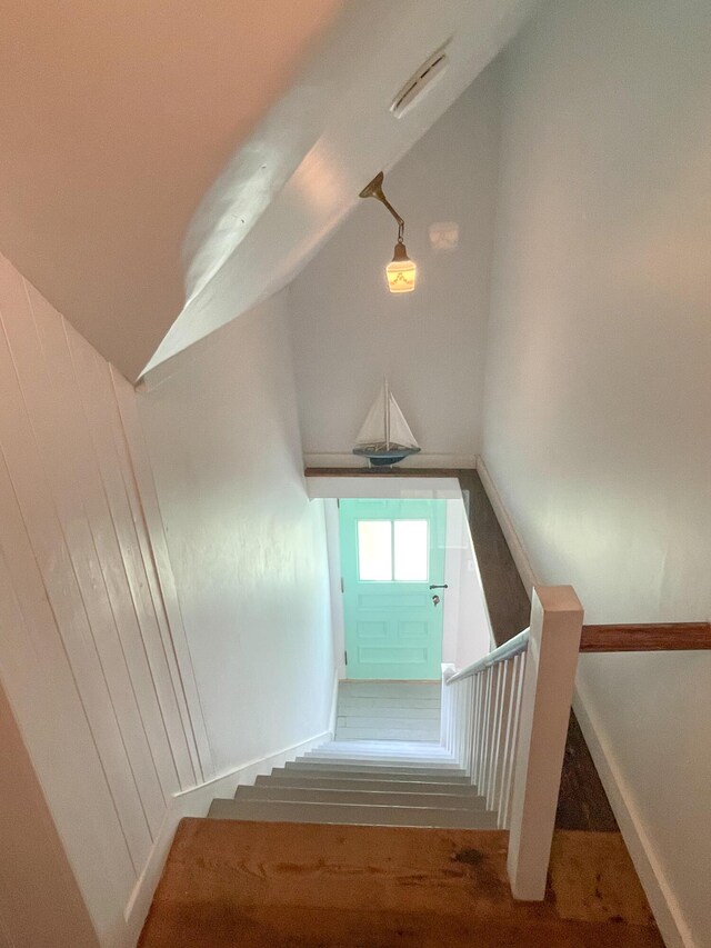 staircase with wood-type flooring, vaulted ceiling, and wooden walls