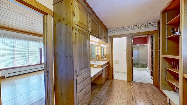 interior space featuring hardwood / wood-style floors, a shower with door, a baseboard heating unit, and vanity