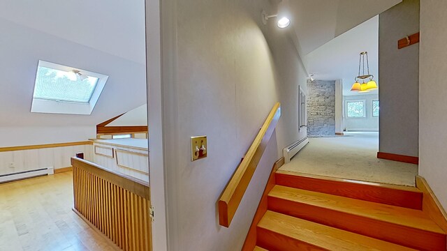 stairs with a baseboard heating unit, high vaulted ceiling, wood-type flooring, and a skylight