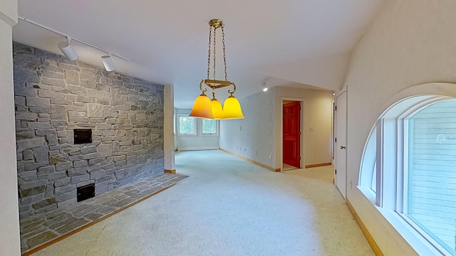 unfurnished dining area with track lighting, a stone fireplace, carpet flooring, and vaulted ceiling