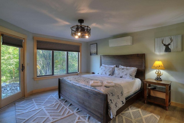 bedroom with a wall mounted AC, wood-type flooring, multiple windows, and access to outside