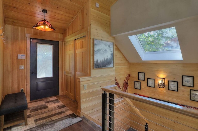 foyer entrance with vaulted ceiling with skylight, hardwood / wood-style flooring, wooden walls, and a healthy amount of sunlight