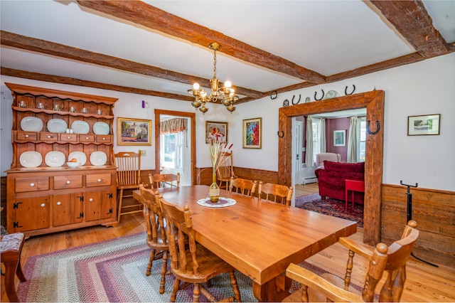 dining room featuring beam ceiling, a healthy amount of sunlight, wood finished floors, and an inviting chandelier