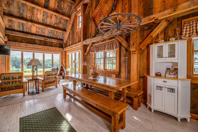 dining area featuring wood walls, light hardwood / wood-style floors, wooden ceiling, and vaulted ceiling with beams