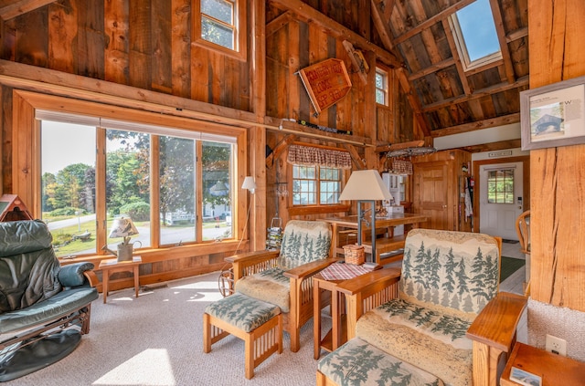 living area featuring wooden walls, a skylight, carpet, and high vaulted ceiling