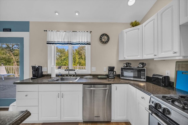 kitchen featuring appliances with stainless steel finishes, sink, white cabinetry, lofted ceiling, and dark stone counters