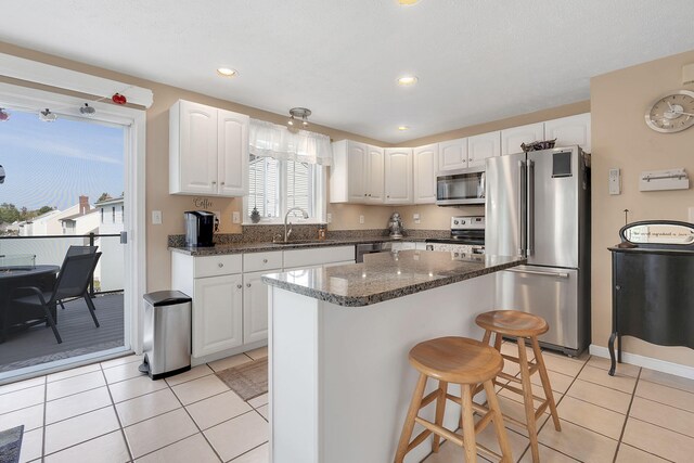 kitchen with appliances with stainless steel finishes, white cabinetry, a kitchen island, light tile patterned floors, and sink