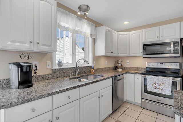 kitchen featuring dark stone countertops, white cabinetry, light tile patterned floors, stainless steel appliances, and sink