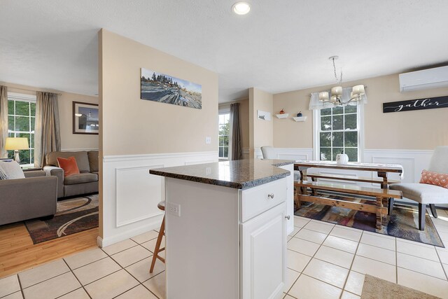 kitchen featuring a wall mounted AC, a wealth of natural light, white cabinetry, and a breakfast bar area