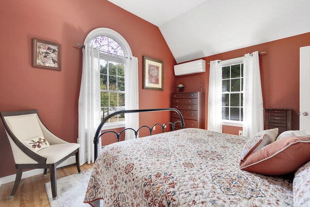 bedroom featuring vaulted ceiling, light hardwood / wood-style floors, and a wall mounted air conditioner