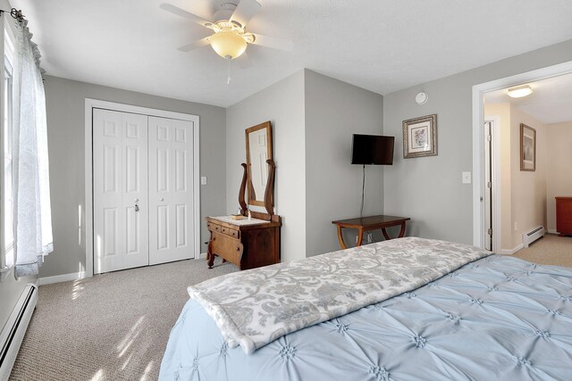 bedroom with a baseboard heating unit, a closet, light colored carpet, and ceiling fan