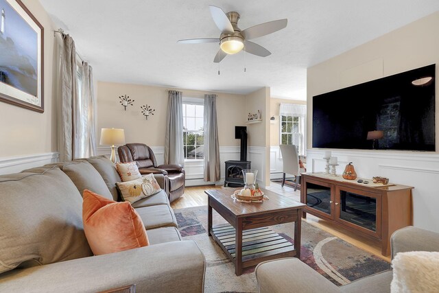 living room with ceiling fan, light hardwood / wood-style floors, and a wood stove