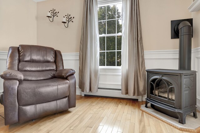 sitting room with a wood stove, baseboard heating, and light wood-type flooring