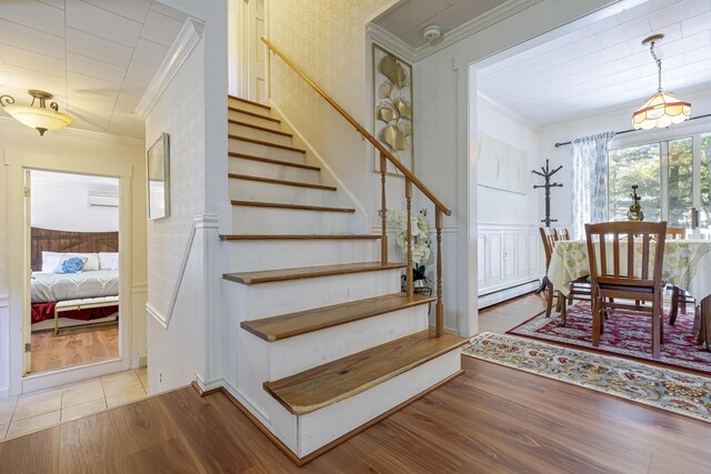 staircase featuring crown molding, baseboard heating, and wood-type flooring