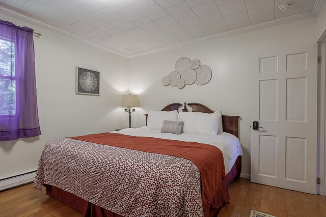 bedroom featuring ornamental molding, hardwood / wood-style flooring, and a baseboard heating unit